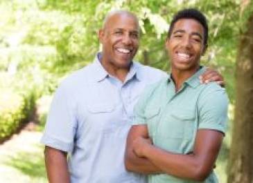 Father standing with his arm over his son's shoulders. Both smiling.
