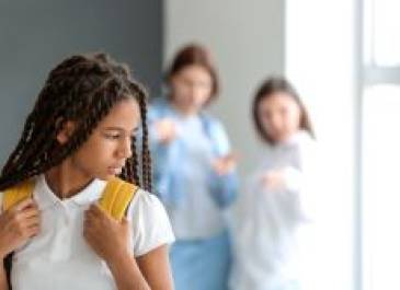 Dark-haired preteen holding the straps of her backpack with her backpack on her back looking over her shoulder at two other preteen girls.