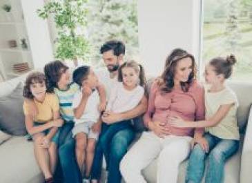 Family sitting on a couch. Mom and dad and five children. Mom is pregnant.