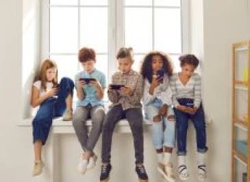 Group of kids sitting on a windowsill looking at their phones.