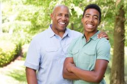 Father standing with his arm over his son's shoulders. Both smiling.