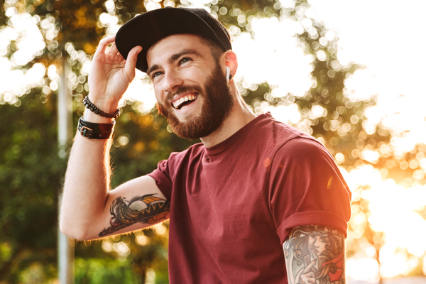 Young male adult with tattoos. Wearing a black hat and a red shirt.