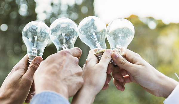 Four human hands holding four lightbulbs