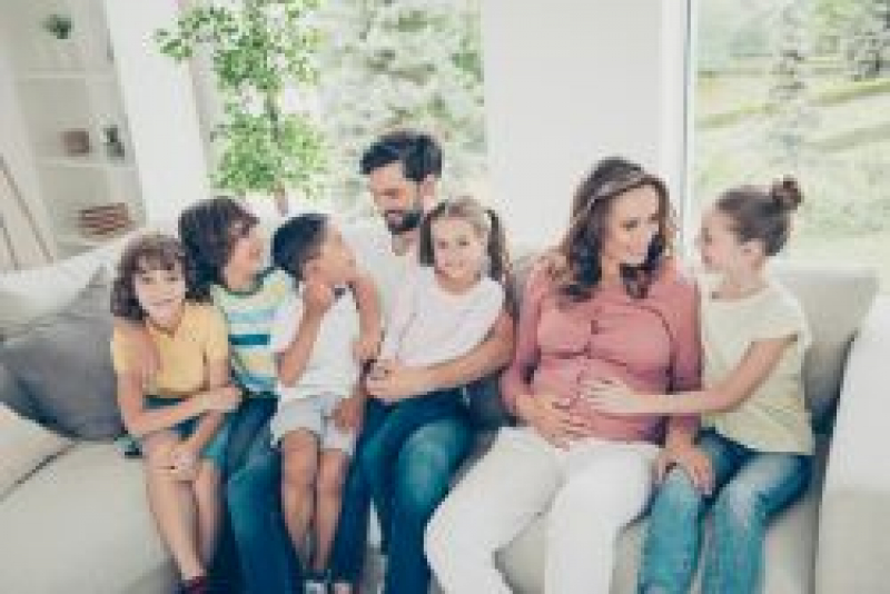 Family sitting on a couch. Mom and dad and five children. Mom is pregnant.