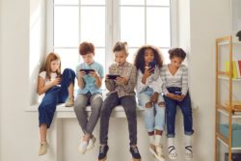 Group of kids sitting on a windowsill looking at their phones.